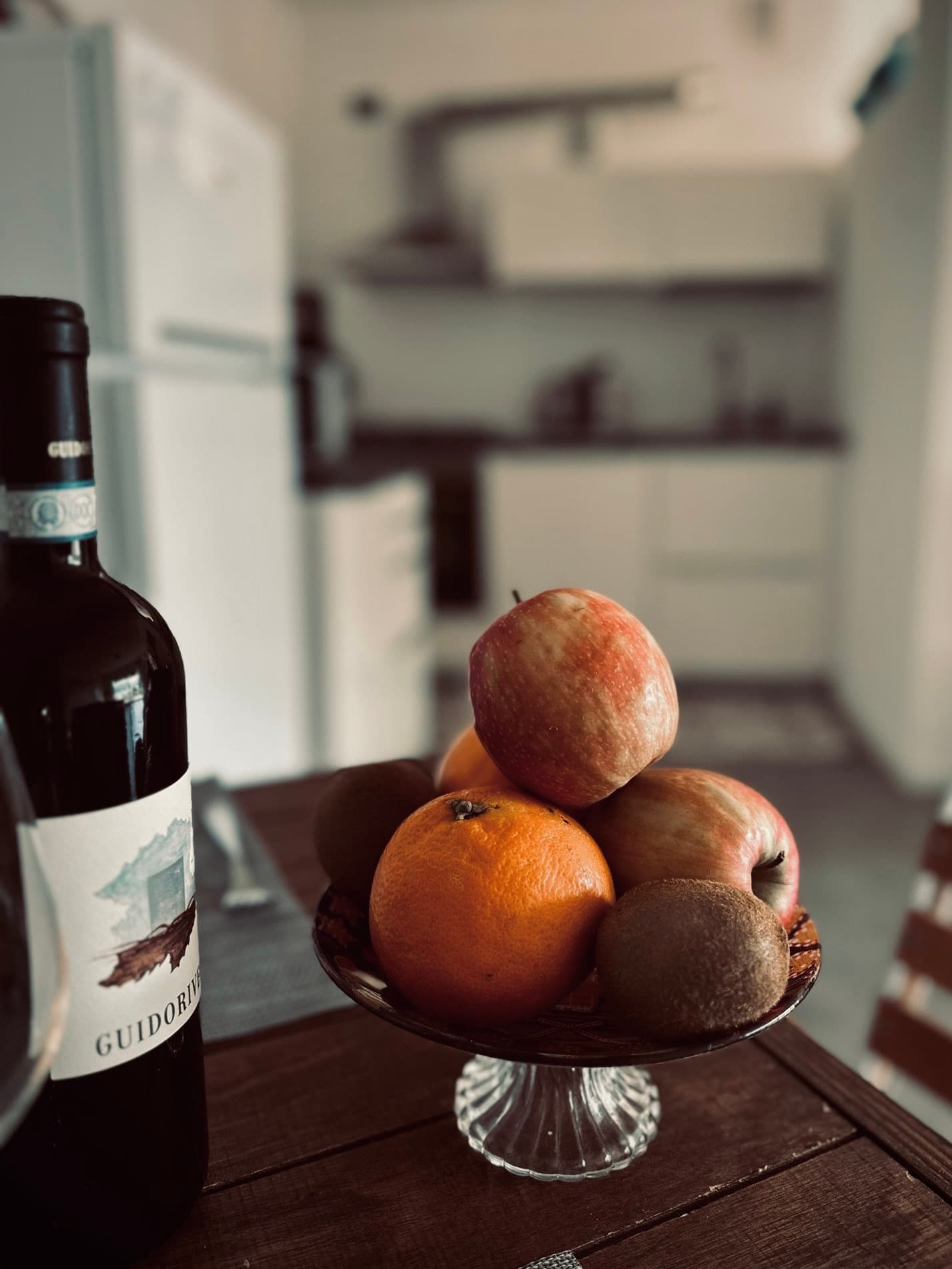 A wine bottle and bowl of fruit on a wooden table